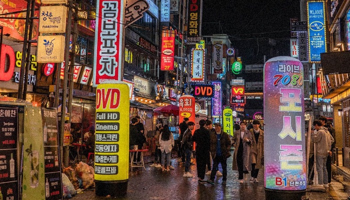 Hongdae Seoul district by night, looking like a real cyberpunk district with commercial ads saturation